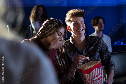 Young couple eating popcorn while watching movie in cinema, laughing.