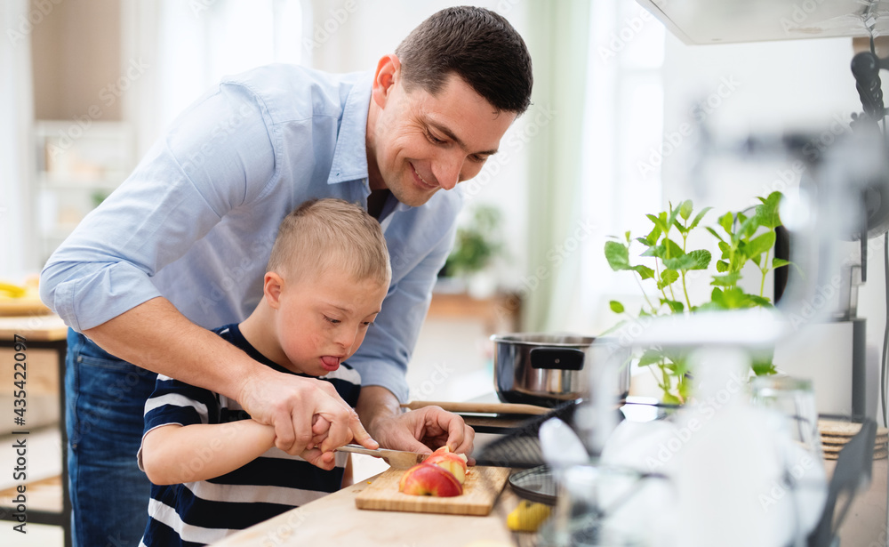Father with happy down syndrome son indoors in kitchen, chopping apple. Father with happy down syndrome son indoors in kitchen, chopping apple.