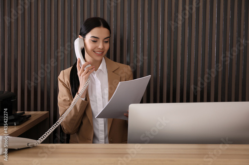 Receptionist with papers talking on phone at countertop in office