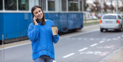 Stylish young girl speaks by phone with takeaway coffee in hand. photo