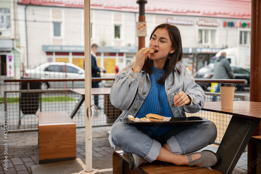 Street portrait of cheerful young woman eating fast food.