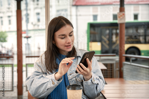 Attractive girl in casual style uses the phone while sitting in a cafe.