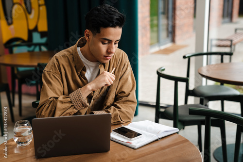 Young hispanic man student sitting at the cafe table indoors © Drobot Dean