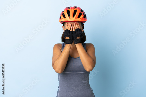 Young cyclist woman isolated on blue background covering eyes by hands