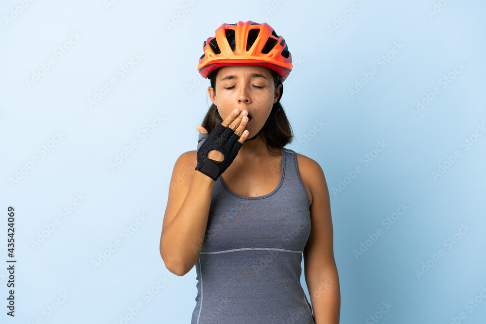 Young cyclist woman isolated on blue background yawning and covering wide open mouth with hand - obrazy, fototapety, plakaty 
