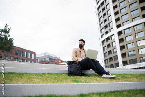 Man with laptop working outdoors in park in city, coronavirus concept.