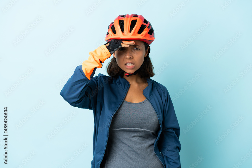 Young cyclist woman isolated on blue background looking far away with hand to look something Young cyclist woman isolated on blue background looking far away with hand to look something