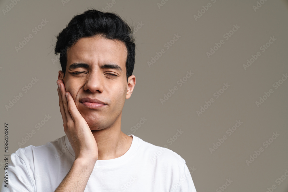 Obraz premium Brunette hispanic man with toothache frowning and rubbing his cheek