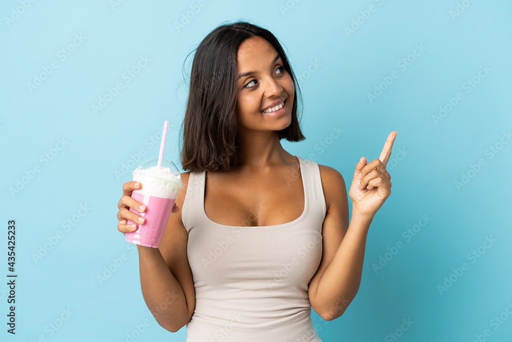 Young woman with strawberry milkshake isolated on blue background pointing up a great idea Young woman with strawberry milkshake isolated on blue background pointing up a great idea