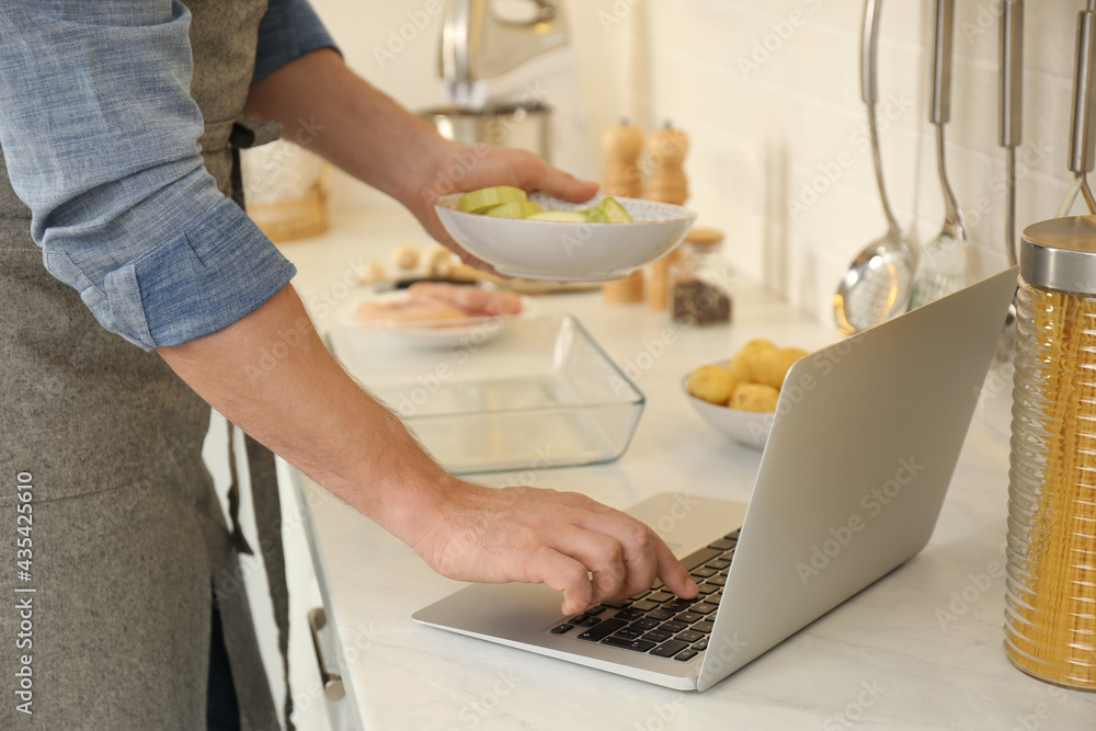 Fototapeta premium Man making dinner while watching online cooking course via laptop in kitchen, closeup