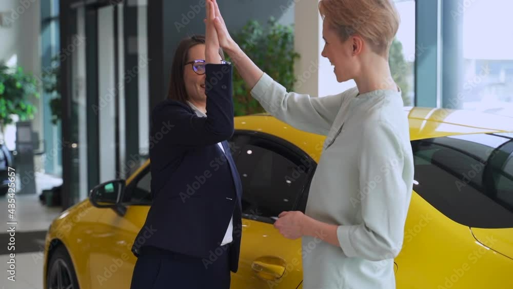 Woman buyer claps hands with seller and takes car keys in dealership office spbas.