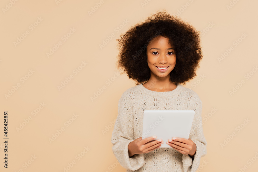 african american preteen girl looking at camera with tablet in hands isolated on beige african american preteen girl looking at camera with tablet in hands isolated on beige