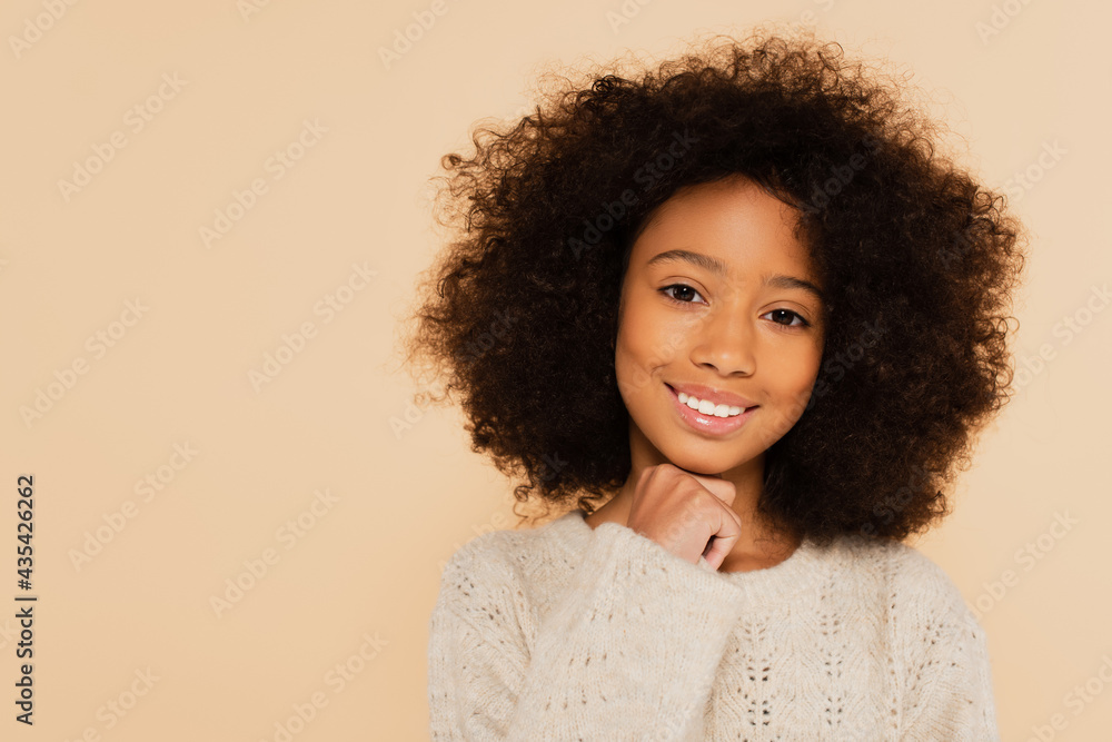 portrait of smiling preteen african american girl with hand near face isolated on beige portrait of smiling preteen african american girl with hand near face isolated on beige
