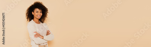 smiling african american woman standing with crossed arms isolated on beige  banner