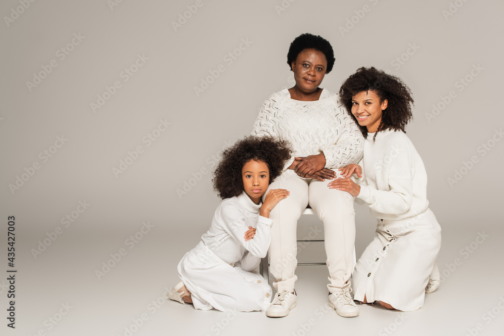 african american daughter and mother sitting on knees near grandmother on grey background african american daughter and mother sitting on knees near grandmother on grey background