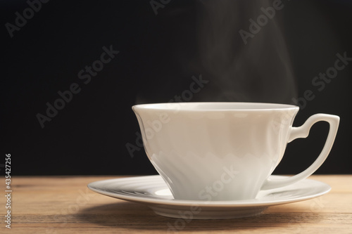 White cup of hot coffee or tea with smoke on wooden table with a black background. Fresh tasty espresso cup of hot coffee.
