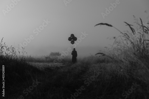 man in a costume of a terrible monster in a Cape with a hood stands in the fog in a field