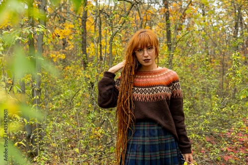 Young woman with red dreadlocks and wearing a sweater in the beautiful autumn forest © serejkakovalev
