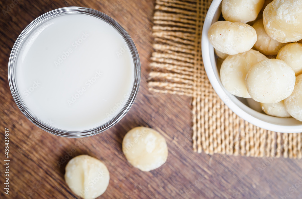 Macadamia milk in a glass and a bowl of macadamia nuts. Macadamia milk in a glass and a bowl of macadamia nuts.