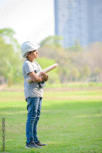 A half-Thai-Indian boy wearing a helmet holds a blueprint And expecting that in the future will be an engineer to build buildings