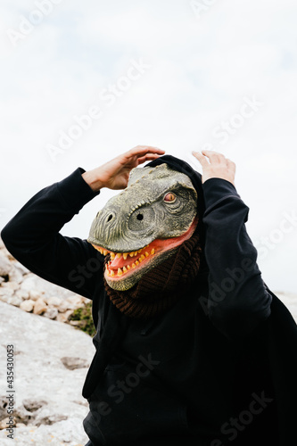 Caucasian man wearing a dinosaur mask and a cape surprised and holding his hands to his head in the Sierra de Tramuntana, Palma de Mallorca, Spain