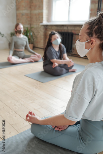 Young yoga trainer in mask showing relaxation exercise to group of girls during practice