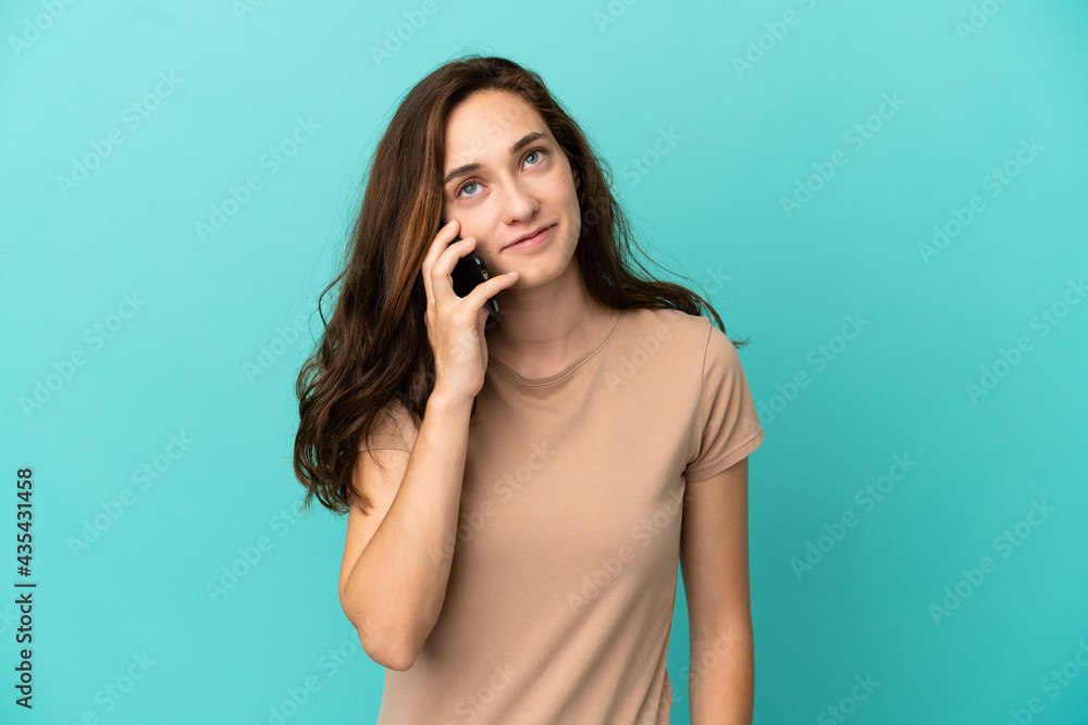 Fototapeta premium Young caucasian woman isolated on blue background keeping a conversation with the mobile phone with someone