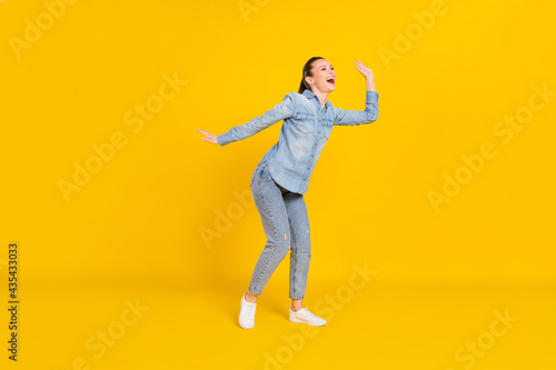 Full length photo of shiny funny young woman wear denim shirt smiling dancing isolated yellow color background