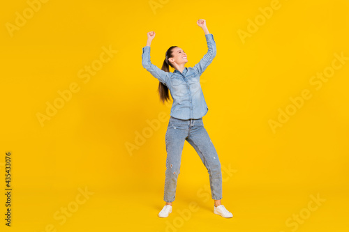 Full length photo of pretty funky young lady dressed jeans shirt jumping smiling isolated yellow color background