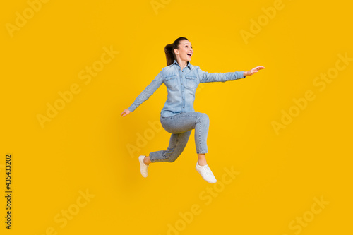 Full body profile side photo of amazed excited young happy woman look run empty space jump up isolated on yellow color background