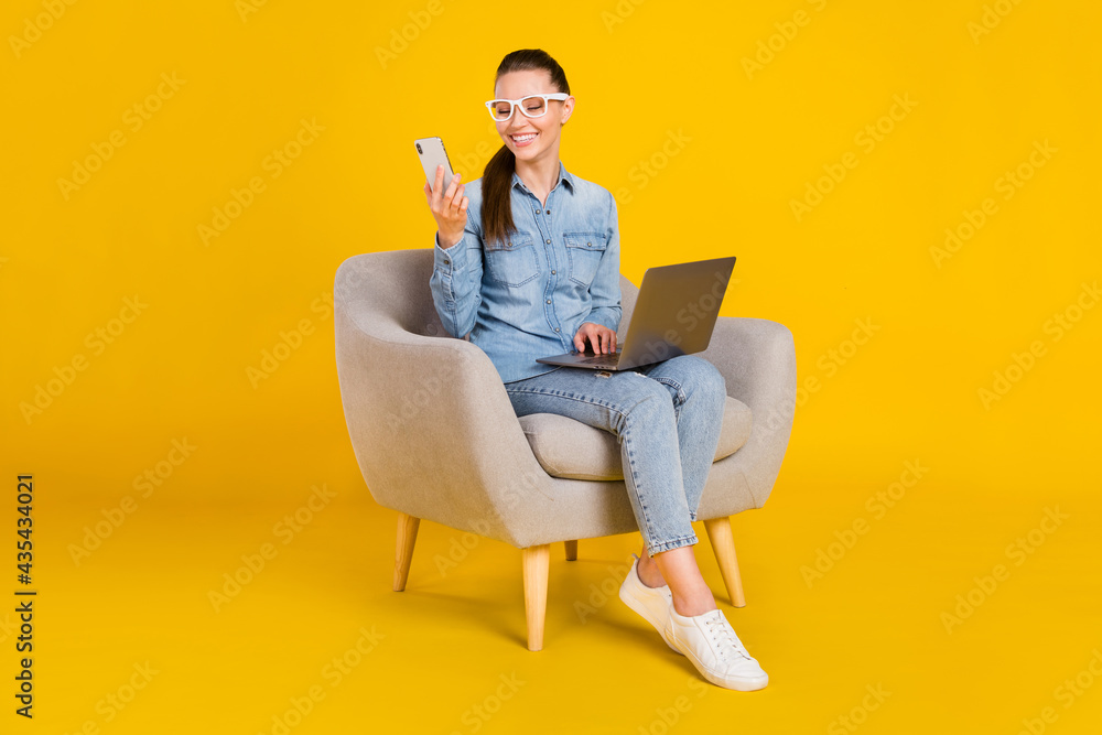 Photo of funny pretty young woman wear denim shirt glasses smiling sitting chair typing modern gadgets isolated yellow color background Photo of funny pretty young woman wear denim shirt glasses smiling sitting chair typing modern gadgets isolated yellow color background