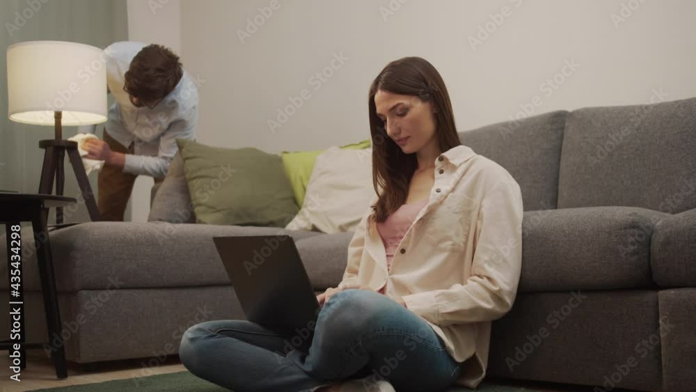 A girl is working on a computer and a man is cleaning in the background. A girl is working on a computer and a man is cleaning in the background.