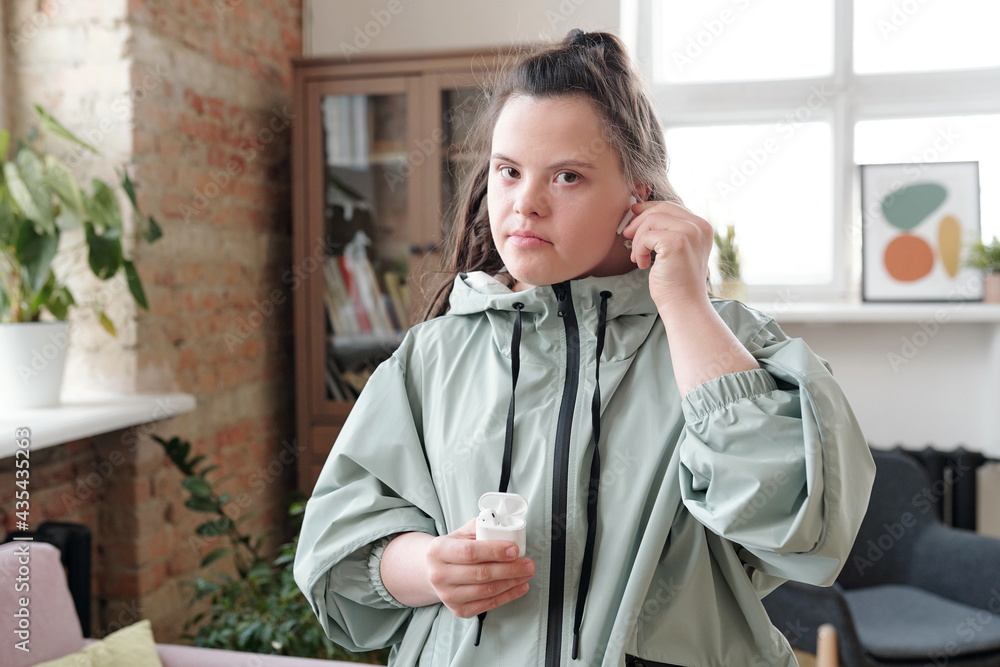 Young sportswoman with Down syndrome putting earphones into ears while going for training Young sportswoman with Down syndrome putting earphones into ears while going for training