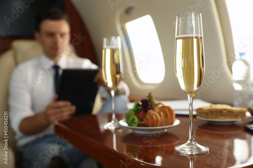 Businessman working at table in airplane during flight, focus on glass of champagne photo