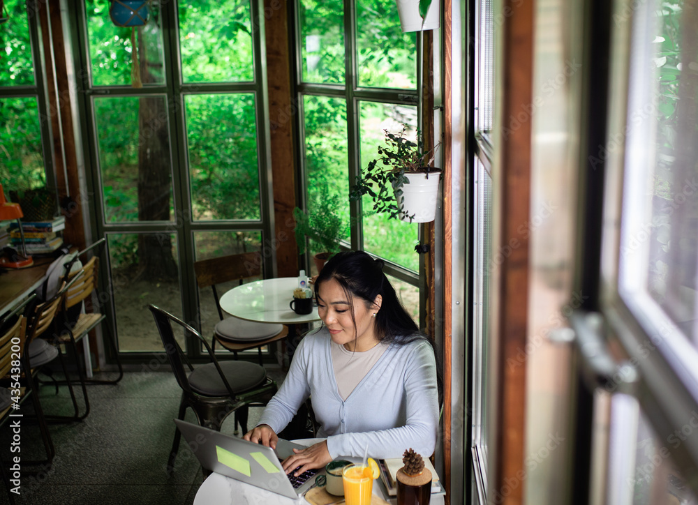 Young Asian woman working in coffee shop using laptop.