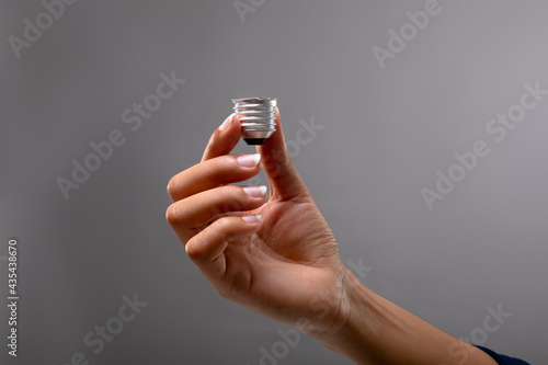 Close up of hand holding bulb screw base against grey background
