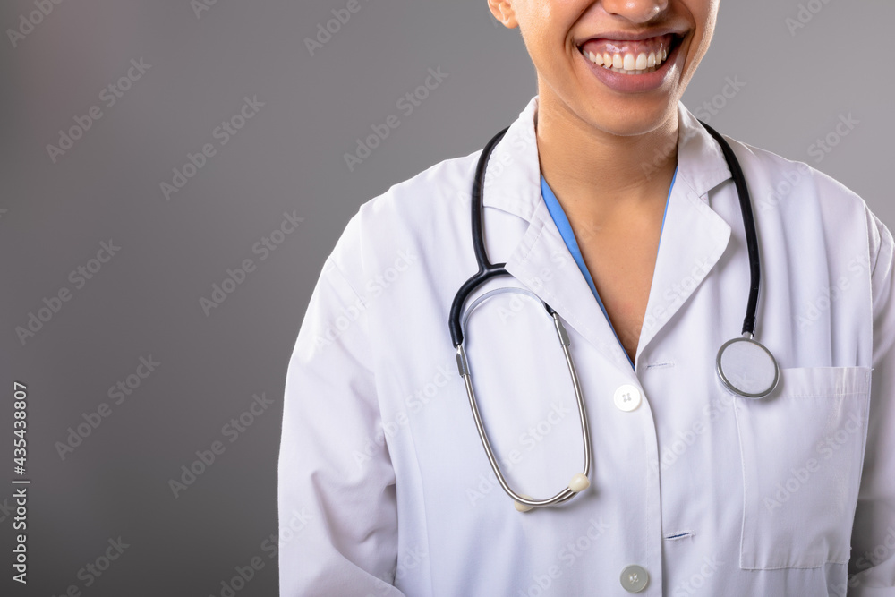 Mid section of african american female doctor smiling against grey background