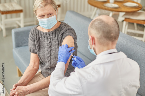 Man doctor vaccinates an elderly woman at her home wearing a protective mask. Vaccination concept