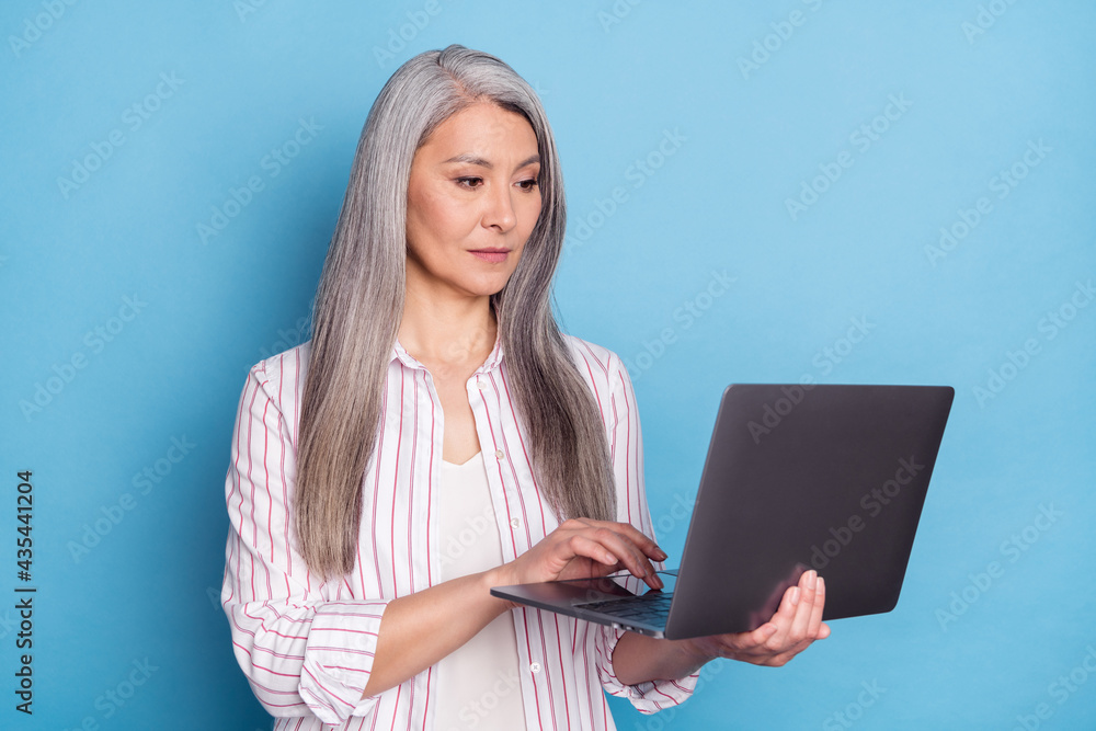 Profile side photo of aged business woman serious look read browse laptop isolated over blue color background Profile side photo of aged business woman serious look read browse laptop isolated over blue color background