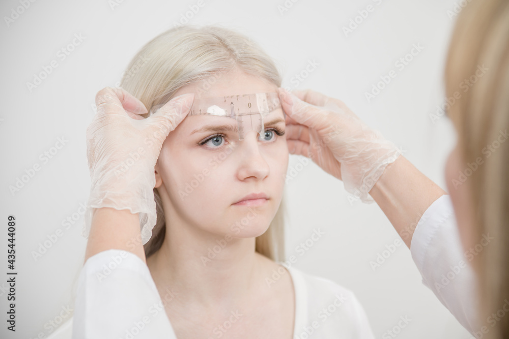 Naklejka premium Young woman having eyebrow correction procedure in beauty salon