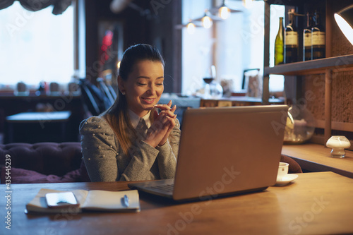 Young beautiful woman sits at a wooden table in a cafe indoors and works on a laptop. Conception of remote work and freelance work.