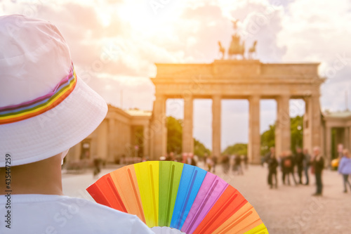 Photography Mature Caucasian LGBT woman in Berlin with rainbow fan and ribbon on white summer hat
