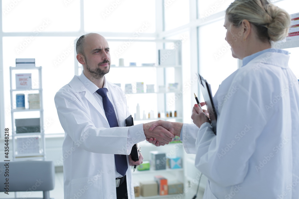 Pharmacists is Working. Man and Woman Handshaking with Each Other. Persons is Smiling. People Wearing Special Medical Uniform. People Located in Pharmacy. Pharmacists is Working. Man and Woman Handshaking with Each Other. Persons is Smiling. People Wearing Special Medical Uniform. People Located in Pharmacy.