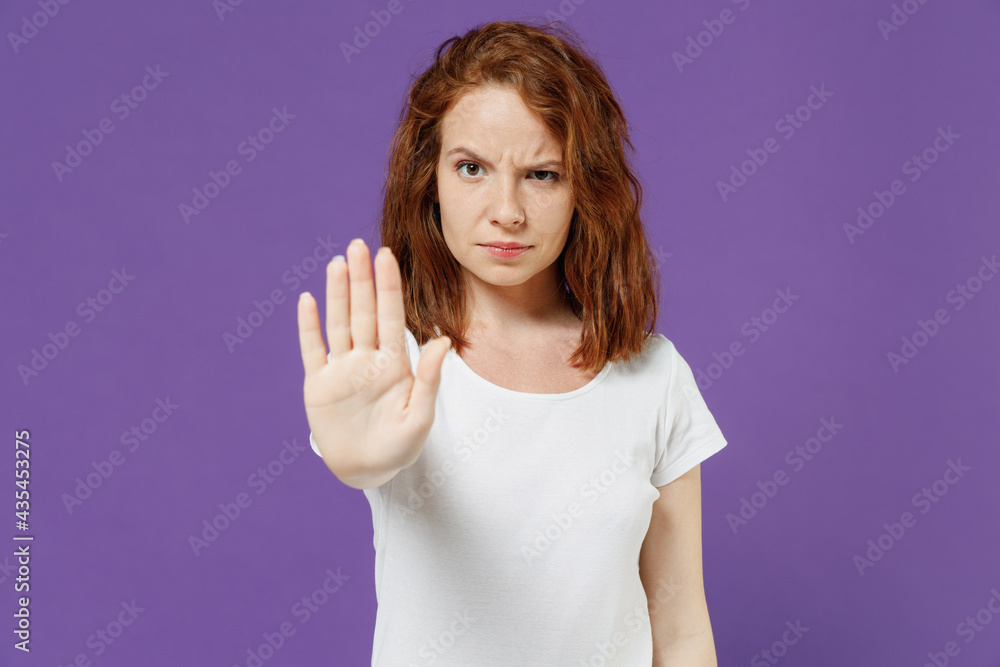 Young sad serious frowning strict caucasian woman 20s wearing white basic blank print design t-shirt doing stop palm gesture refusing say no isolated on dark violet color background studio portrait Young sad serious frowning strict caucasian woman 20s wearing white basic blank print design t-shirt doing stop palm gesture refusing say no isolated on dark violet color background studio portrait