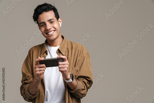 Brunette hispanic man smiling while using cellphone and earphones © Drobot Dean