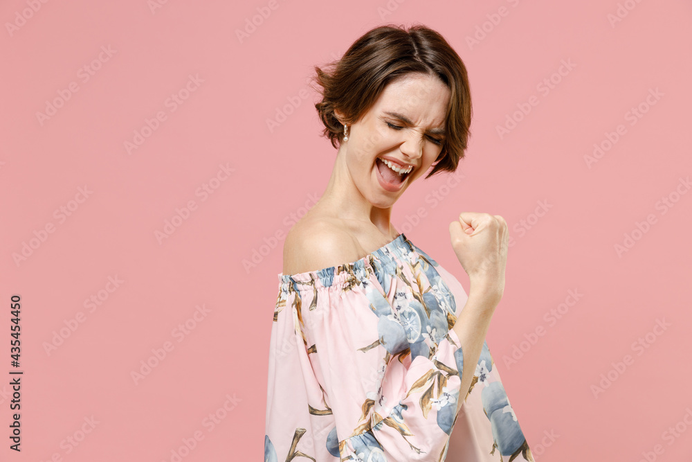Young side view overjoyed happy stylish woman 20s with short hairdo in trendy blouse do winner gesture clench fist scream isolated on pastel pink background studio portrait. People lifestyle concept. Young side view overjoyed happy stylish woman 20s with short hairdo in trendy blouse do winner gesture clench fist scream isolated on pastel pink background studio portrait. People lifestyle concept.