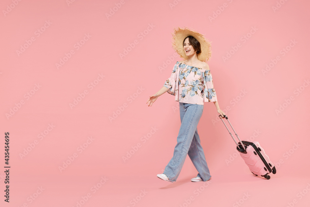 Traveler tourist fun woman 20s in summer casual clothes, hat hold suitcase valise walk go isolated on pastel pink background Passenger traveling abroad on weekends getaway. Air flight journey concept Traveler tourist fun woman 20s in summer casual clothes, hat hold suitcase valise walk go isolated on pastel pink background Passenger traveling abroad on weekends getaway. Air flight journey concept