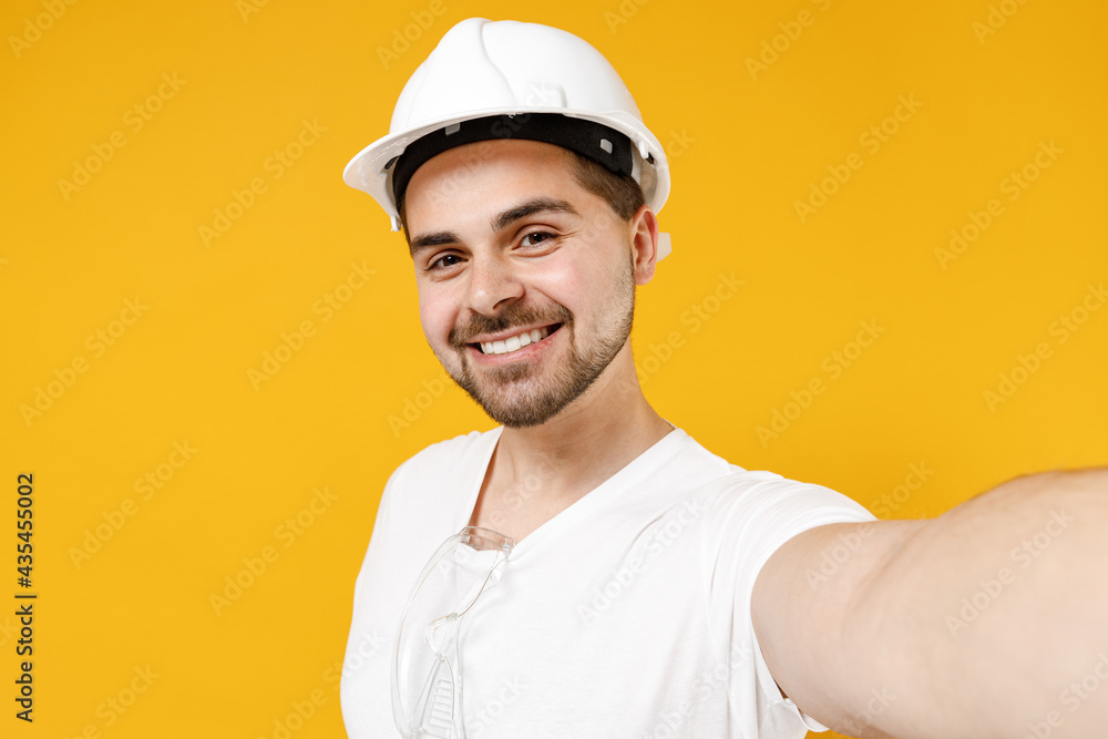 Close up young employee handyman man in protective helmet hardhat doing selfie shot on mobile phone isolated on yellow background Instruments accessories renovation apartment room Repair home concept