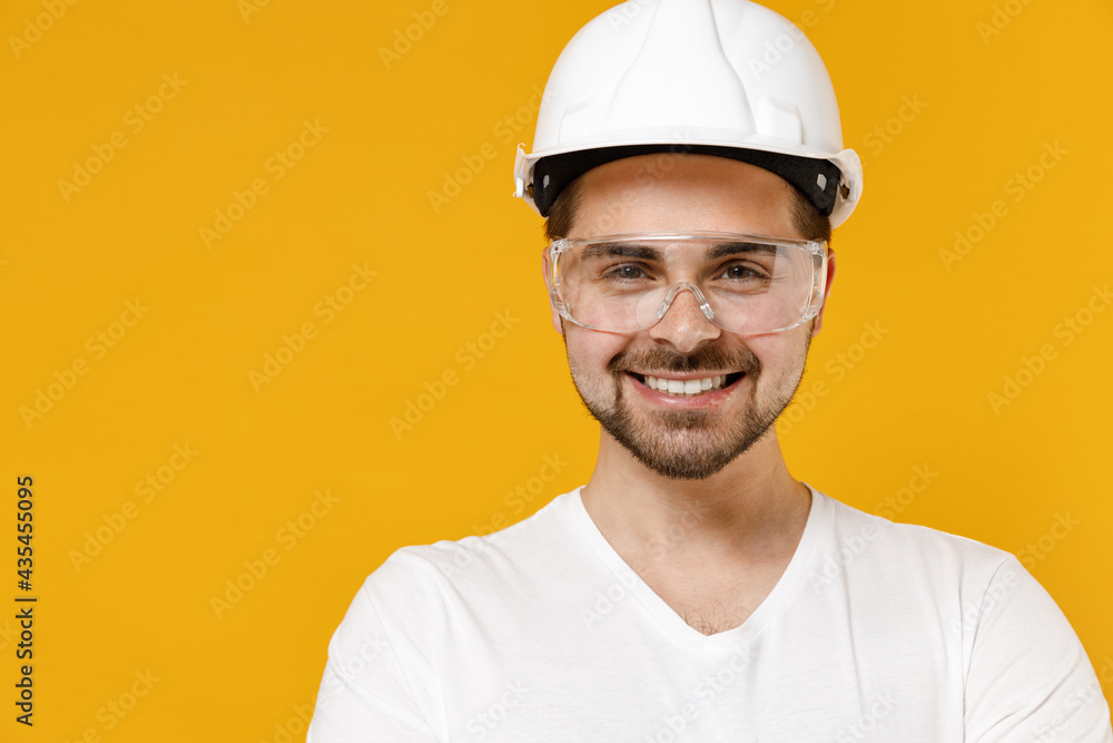 Close up young employee handyman man in protective helmet hardhat glasses loking camera isolated on yellow background studio. Instruments accessories renovation apartment room. Repair home concept