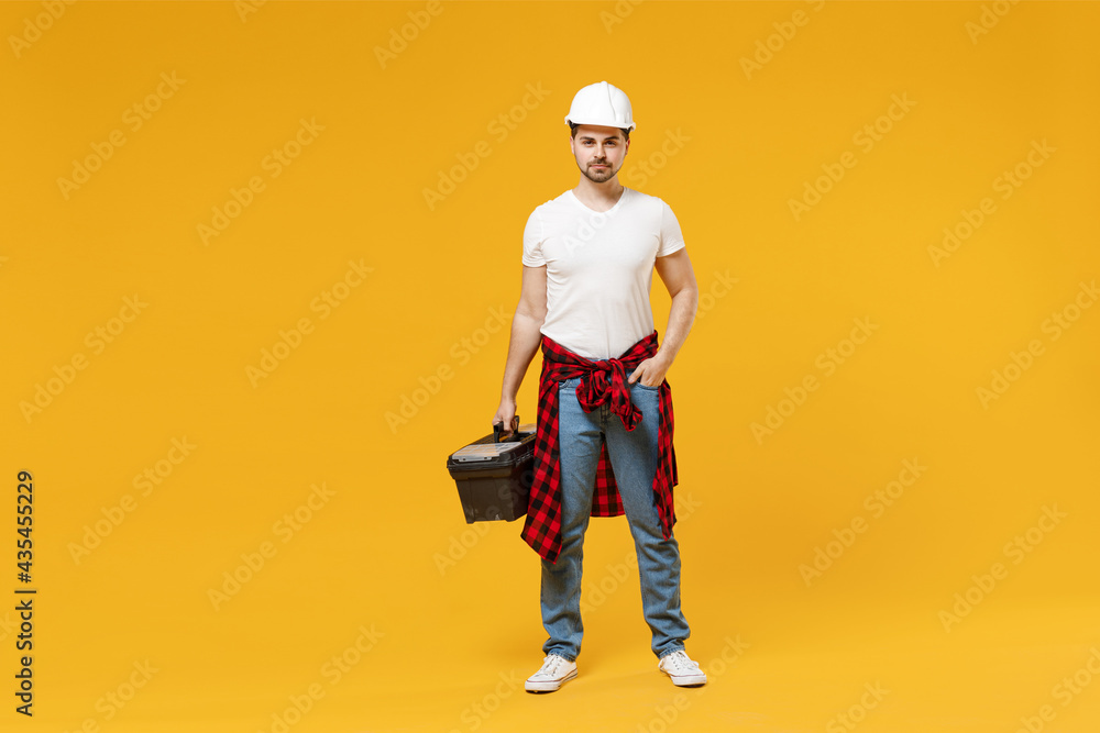 Full length young fun excited employee handyman man 20s in protective helmet hardhat tool case box isolated on yellow background Instruments accessories renovation apartment room Repair home concept.